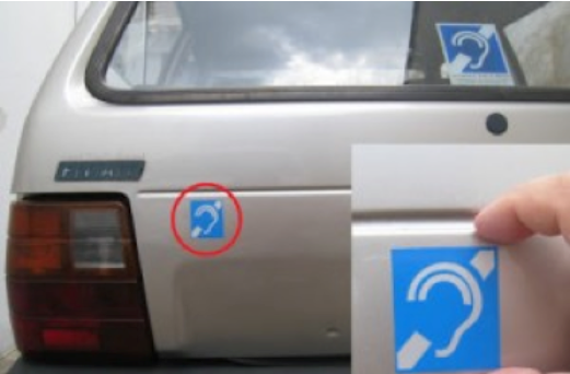 Foto da traseira de um carro com um adesivo do símbolo da surdez.