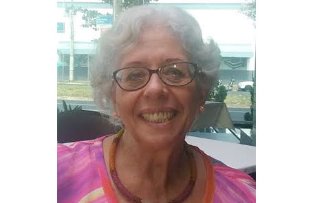 Descrição da Imagem: Fotografia de Marta Gil, uma mulher de óculos e com cabelos brancos e curtos. Veste uma blusa com tons de rosa e lilás e está sorrindo.