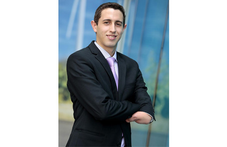 Descrição de Imagem: Fotografia de Daniel Paz, trabalhador do Citibank. É um homem branco de cabelos escuros e curtos. Veste um terno escuro e usa gravata. Na foto está sorrindo e com os braços cruzados, a manga do paletó do braço esquerdo é mais curta, de forma que podemos ver a deficiência do seu antebraço