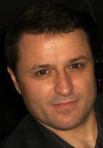 Descrição de imagem: Fotografia do rosto de Fábio Uzunof. Fábio pe um homem branco, de cabelos curtos e escuros e veste uma camisa preta.