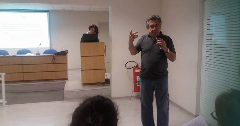 Descrição de Imagem: Fotografia do Dr. José Carlos do Carmo, coordenador da Câmara Paulista para Inclusão. Ele está de pé e fala ao microfone. É um homem de cabelos grisalhos e óculos, veste uma camisa polo preta e calça jeans.