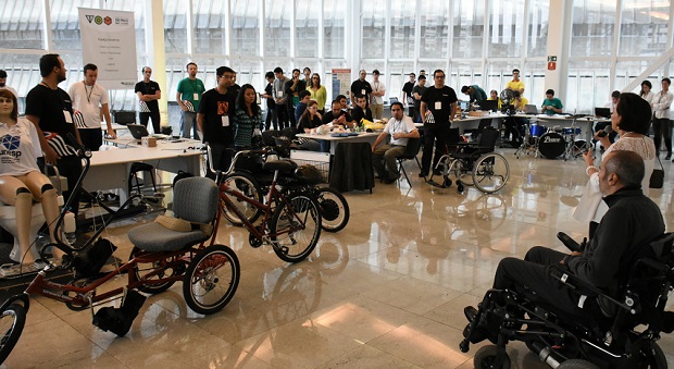 Descrição de Imagem: Fotografia do evento TOM São Paulo. Um grande saguão com vários expositores distribuídos em várias mesas que mostram inovações tecnológicas na área de tecnologia de mobilidade. Ao lado direito está Cid Torquato, secretário adjunto da Secretaria dos Direitos da Pessoa com Deficiência do Estado de São Paulo. É um homem cadeirante, com cabelos grisalhos. Veste uma blusa e calça pretas.