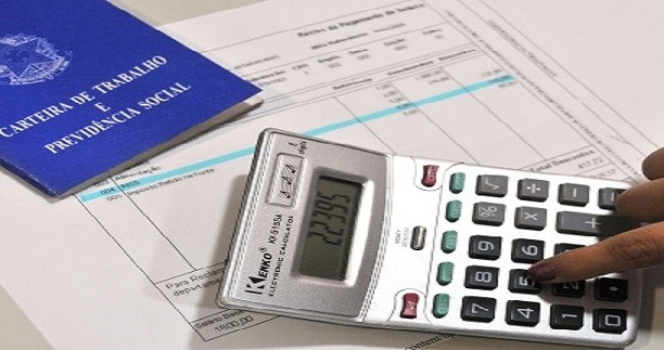 Descrição de Imagem: Fotografia de um recibo de pagamento em cima de uma mesa, sobre o papel está uma carteira de trabalho e uma calculadora