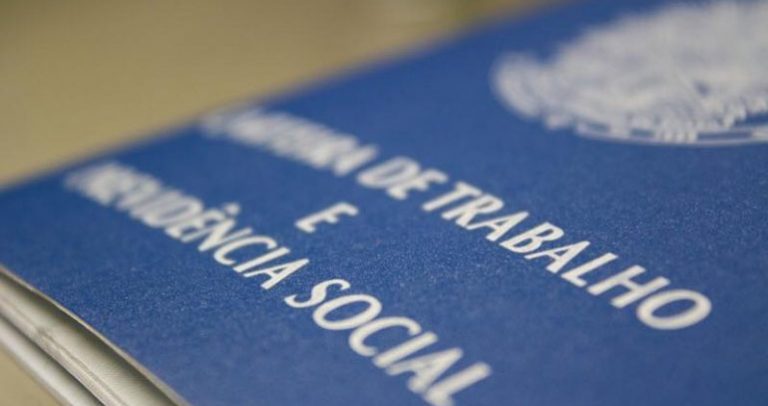 Descrição de Imagem: Fotografia de uma carteira de trabalho, uma carteira azul escrito em branco Carteira de Trabalho e Previdência Social