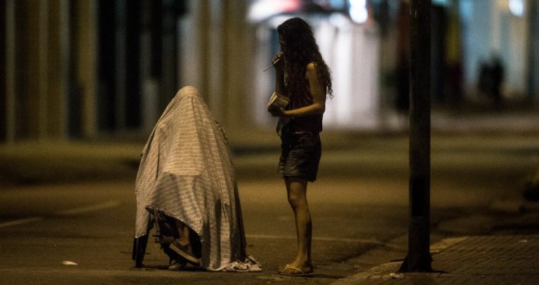 Descrição da imagem: Cadeirante coberto por um lençol é acompanhado por uma mulher que fuma crack