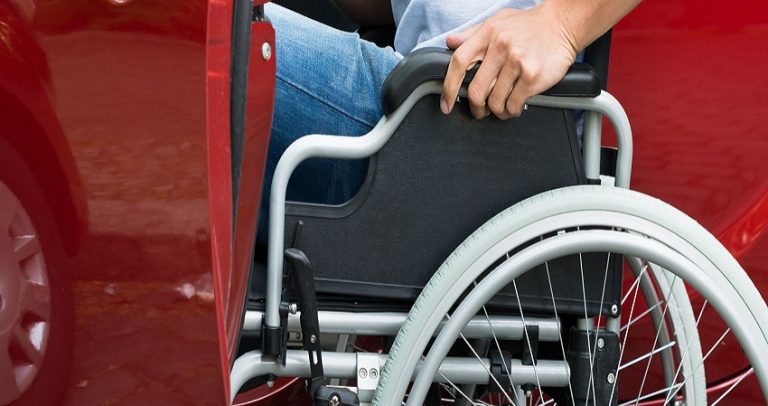 Descrição da imagem: cadeirante entrando em um carro, no lugar do motorista. O carro é vermelho.