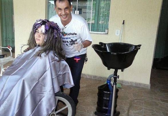 O cabeleireiro atende uma mulher cadeirante. Ela está fazendo mechas no cabelo. José Valente sorri enquanto faz o trabalho.