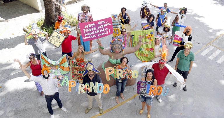 Descrição da imagem: pessoas fantasiadas carregam bonecos carnavalescos e cartazes com o nome do bloco Tá Pirando, Pirado, Pirou!