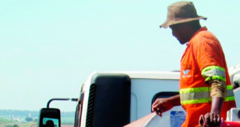 Foto de um trabalhador que está em cima de um caminhão, vestido com uniforme cor de laranja.