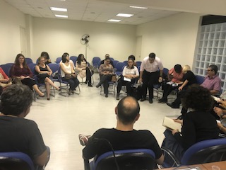 Fotos do grupo de trabalho. Todos estão sentados em cadeiras que formam um grande círculo, de aproximadamente 30 pessoas.