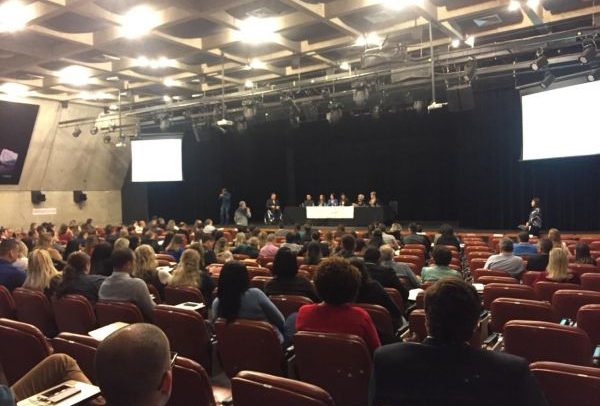 foto do público em auditório, onde se vê ao fundo a mesa com representantes do MPT e MTb