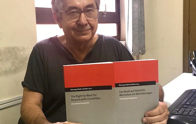 Na foto, Dr. José Carlos do Carmo, Kal, segura as duas edições do livro, uma escrita em Inglês e a outra em Alemão. Ele está sorrindo. As capas são nas cores vermelha, cinza e preto.