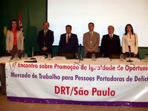 Descrição da foto: seis pessoas, entre elas Guibe (ex-superintendente), Maurinho (ex-vice super.) e Newton (na época estava em Brasília, no MTb), estão de pé atrás de uma mesa de eventos onde há uma grande faixa com o texto: 1º Encontro sobre Promoção de Igualdade de Oportunidades no Mercado de Trabalho para Pessoas Portadoras de Deficiência / DRT São Paulo (obs: o termo "portadores" ainda era usado, e a expressão "pessoa com deficiência" passou a ser difundida após a Convenção da ONU, em 2006)