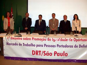 Descrição da foto: seis pessoas, entre elas Guibe (ex-superintendente), Maurinho (ex-vice super.) e Newton (na época estava em Brasília, no MTb), estão de pé atrás de uma mesa de eventos onde há uma grande faixa com o texto: 1º Encontro sobre Promoção de Igualdade de Oportunidades no Mercado de Trabalho para Pessoas Portadoras de Deficiência / DRT São Paulo (obs: o termo "portadores" ainda era usado, e a expressão "pessoa com deficiência" passou a ser difundida após a Convenção da ONU, em 2006)