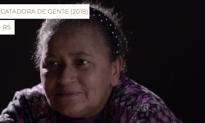 Foto da "Catadora de Gente" Maria Tugira Cardoso, uma senhora de cabelos grisalhos presos. Ela está em um ambiente pouco iluminado.