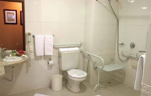 foto de um banheiro com recursos de acessibilidade na área de banho, vaso sanitário e pia.