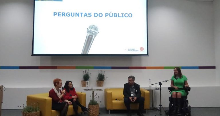 Uma foto onde estão, no palco, Cristina Masieiro, Ivone Santana, Dr. José Carlos do Carmo, Kal, e a deputada federal Mara Gabrilli. O palco tem 2 sofás pequenos e amarelo, e a deputada Mara Gabrilli, que usa cadeira de rodas, está falando ao microfone. No alto aparece o telão com a frase Perguntas do Público.