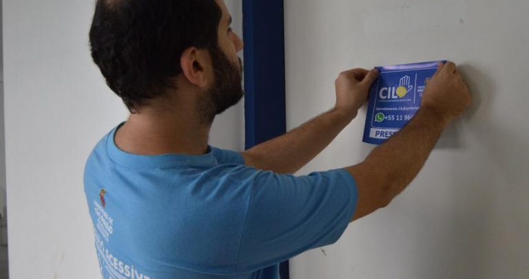 o assessor técnico da SMPED Eduardo Jurado colando um dos adesivos da CIL, em uma porta branca.