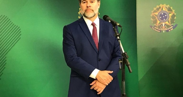 Foto do Ministro Dias Toffoli, de pé, com terno azul marinho, camisa branca e gravata vermelha. Ele tem barba grisalha.