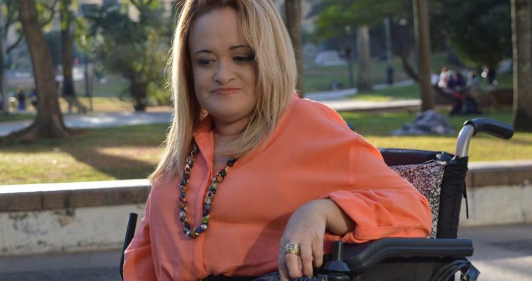 #pracegover #paratodosverem: sentada em sua cadeira de rodas, Ivone faz pose para o fotógrafo. Fim da descrição