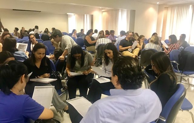 grupo de participantes, aproximadamente 60 pessoas, sentados em cadeiras em formato de vários círculos.