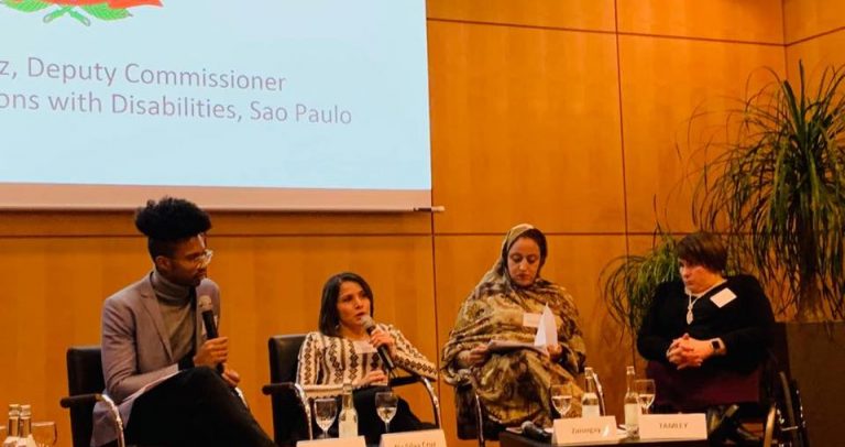 Secretária Adjunta da SMPED, Marinalva Cruz, fala ao microfone ao lado de representantes de outros países. Atrás tem um telão com a apresentação da Prefeitura de São Paulo.