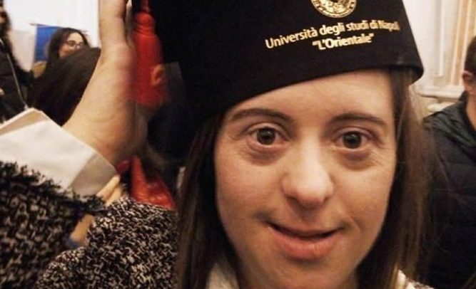 Foto do rosto de Giulia sorridente, segurando chapéu sobre sua cabeça, com o nome da universidade.