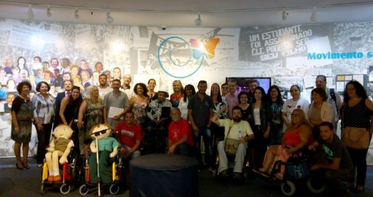 grupo de sindicalistas posam para foto durante visita ao Memorial da Inclusão, tendo a frente dois bonecos sentados em suas cadeiras de rodas