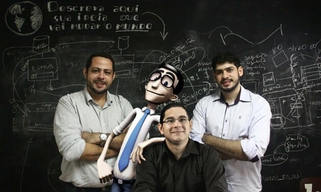 Brasileiros posam com o personagem Hugo em frente a uma lousa negra escrita em giz branco