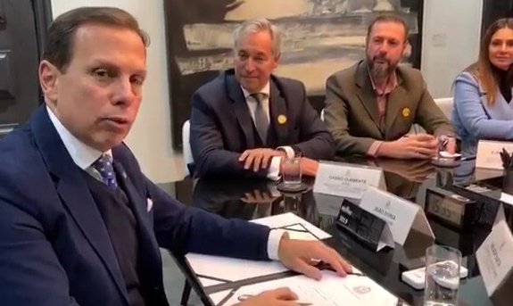 Fotografia mostra o governador de São Paulo, João Dória assinando o documento que aprova a contratação de jovens com deficiência. Três pessoas observam