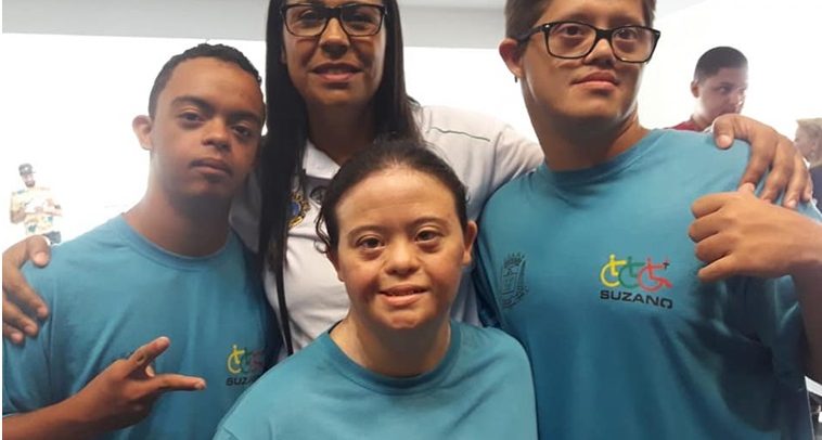 Fotografia mostra técnica abraçado com os seus três atletas. Os nadadores vestem camiseta azul com a logomarca da equipe