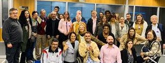 Fotografia mostra um grupo de pessoas, algumas de pé e outras sentadas. Do lado esquerdo da foto, Kal, Valdirene e Clemente