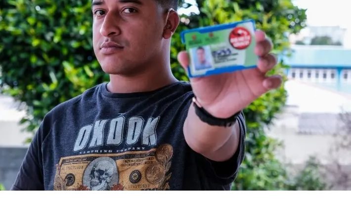 Foto de Bruno Pompeu, de 26 anos. O jovem é negro, tem cabelos curtos e olha para frente com um semblante sério. Ele segura um cartão do Bilhete Único Especial com a mão esquerda e tem um aparelho auditivo no ouvido esquerdo.