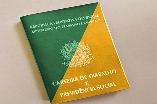 Foto da carteira nacional do trabalho apoiado. Ela está em uma mesa branca e é pintada metade de amarelo e metade de verde.