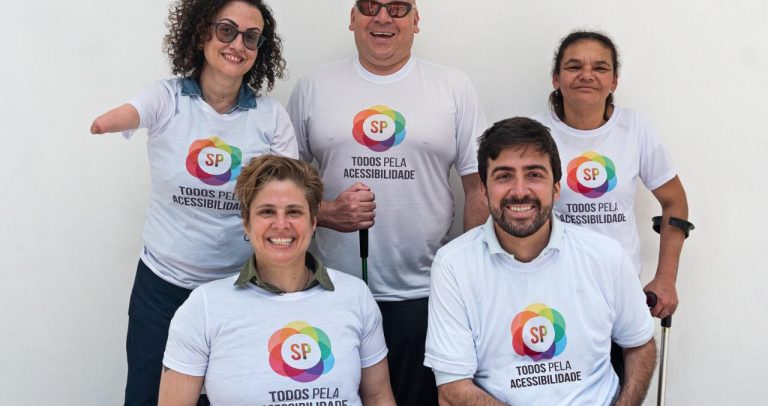 Foto com os 5 integrantes sorrindo, de pé da esquerda pra direita, Carol Paraguaçu fazendo uso de próteses nas pernas, Sonny Polito deficiente visual usa sua bengala, e Maria de Fátima fazendo uso de muletas. Sentados em suas cadeiras de rodas estão Selma Rodeguero, paraplégica, e Bruno Beraldin, tetraplégico que usa cadeira de rodas motorizada.