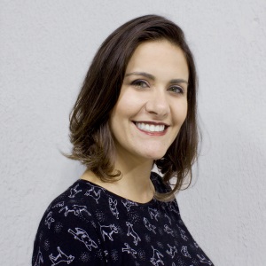 Foto de Meire Cavalcante, uma das palestrantes do evento. Ela é uma mulher branca, de olhos e cabelos castanhos escuros, lisos e cortados na altura no ombro. Usa uma blusa preta com detalhes em branco. Meire está sorrindo.