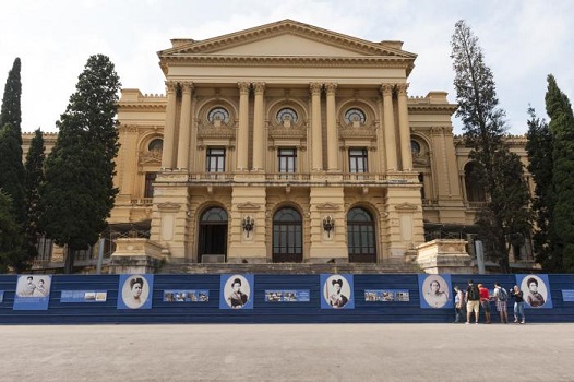 imagem da fachada do museu do ipiranga, um prédio em tom bege, sustentado por 4 colunas frontais e janelas em estilo colonial, com vários arbustos à sua volta