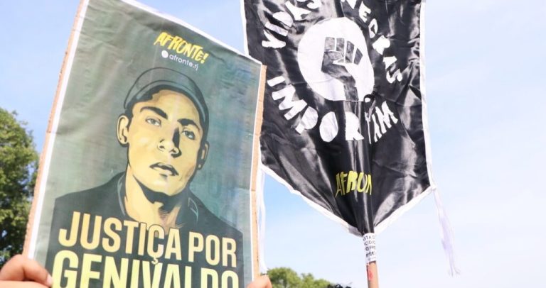 Duas bandeiras erguidas em manifestação. Em uma delas está escrito: Justiça por Genivaldo, com a foto dele. Na outra está escrito: Vidas negras importam.