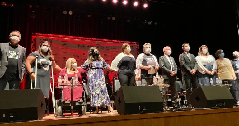 Foto mostra todos os convidados que tiveram sua fala descrita na notícia. Eles e elas estão no palco.