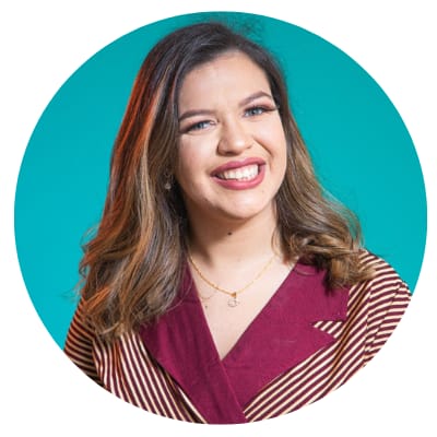 Aline é uma mulher de pele branca, olhos verdes, cabelos longos e lisos, de cor castanho claro. Está maquiada e sorrindo, usa uma blusa com gola cor de vinho e listras vinho e bege.