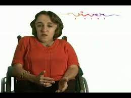 foto de Leandra em 2006, na abertura da novela Páginas da Vida. Ela tem a pele branca, cabelos lisos castanhos cortados acima dos ombros, olhos castanhos, usa blusa vermelha e está sentada na cadeira de rodas.