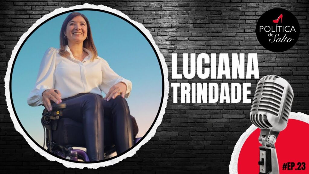 foto de Luciana Trindade. Ela tem a pele branca, cabelo marrom longo e liso, olhos castanhos, usa camisa branca, calça preta e está sentada na cadeira de rodas. Está sorrindo.