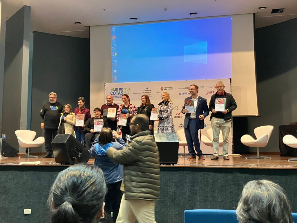 homenageados do ano estão de pé no palco, lado a lado, segurando a placa de reconhecimento.