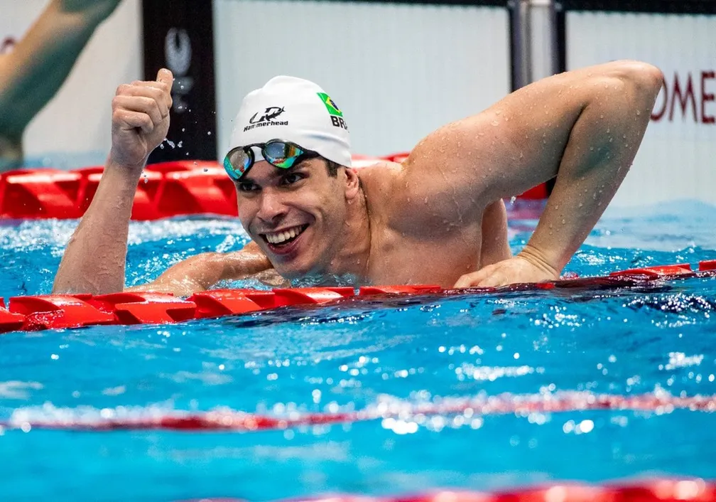 Phelipe Rodrigues é um homem branco de olhos castanhos. Na foto está nadando em uma piscina com raias, e aparecem seus braços e tronco em movimento de natação. Está sorrindo.