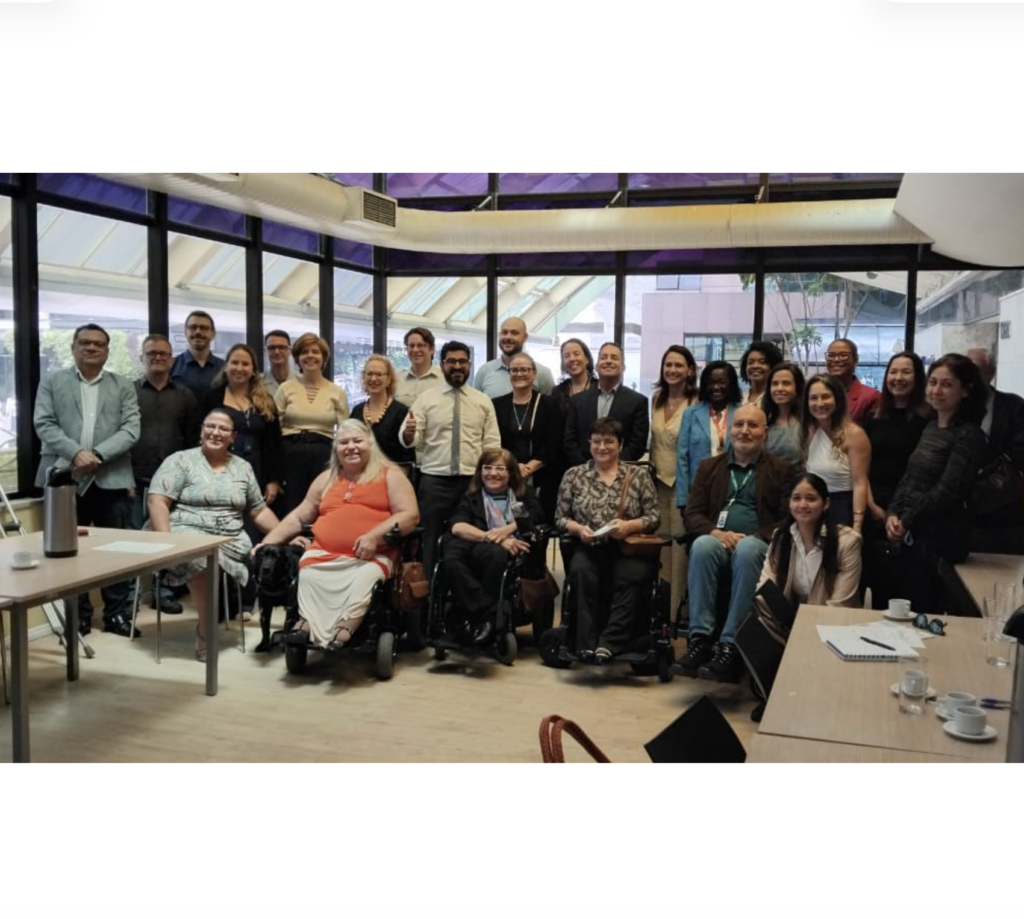 Foto do grupo de integrantes do Fórum Paulista de Acessibilidade e Inclusão, com todos os participantes da reunião de 2026. Algumas pessoas estão posicionadas de pé, outras estão em cadeiras de rodas. Uma das pessoas tem um cão guia.